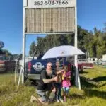 Matt posing with LB and Statia our October 2023 Citrus County Umbrella Winner they are standing in front of the BAMM sign in Inverness FL