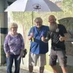 Matt standing with Mike and Elenor our November 2023 Citrus County Umbrella Winner, they are standing in front of the mural on the building at Floral City Hardware